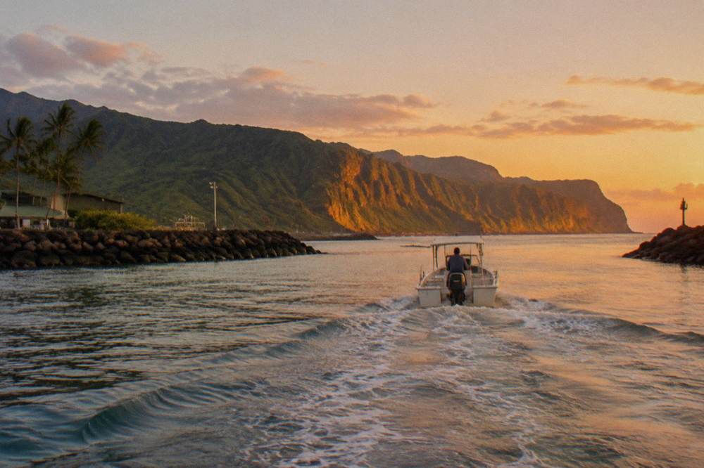 A boat underway on calm water below the eroded green walls of the Na Pali coast